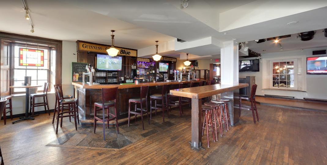An event space in a pub with a large wooden bar, high-top tables, and flat-screen TVs at The Olde Stone Cottage Pub.