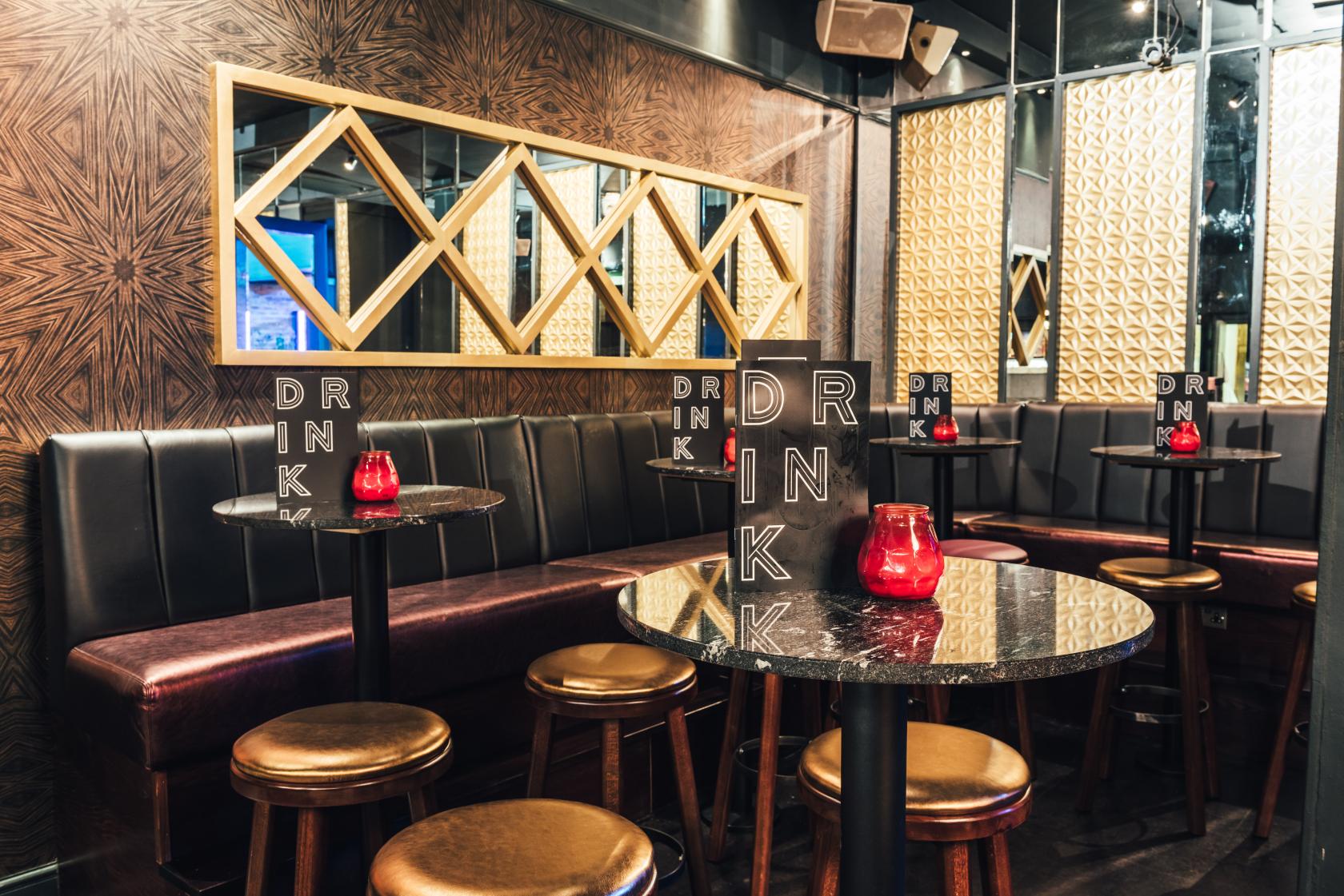 An intimate event space with mirrored walls, black leather banquettes, round marble tables, and red candle holders at Sway.