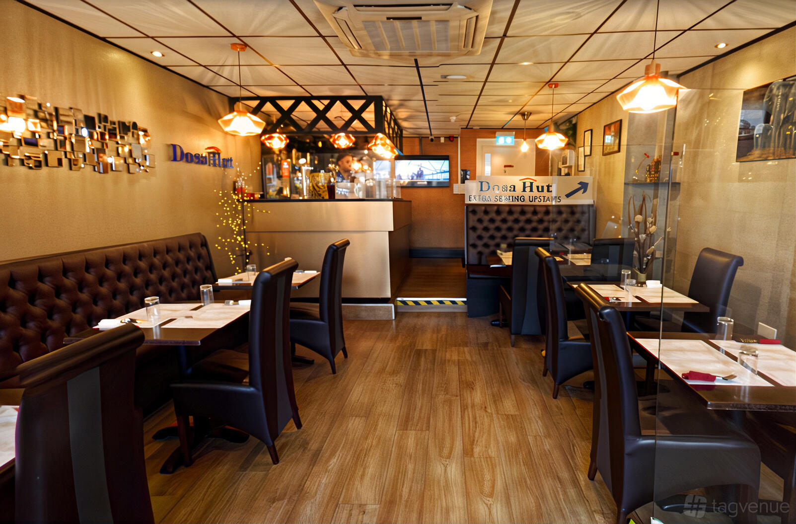 An event space in a restaurant with dark leather chairs, wooden floors, and pendant lighting at Dosa Hut.
