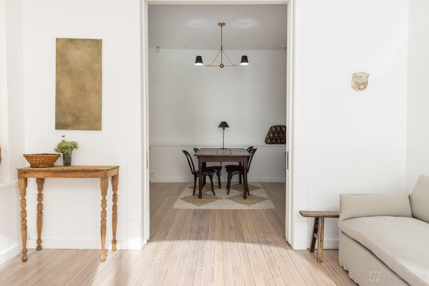 A photo studio with light wood floors, white walls, and a central table with black chairs at Ashleigh Amoroso Studio.