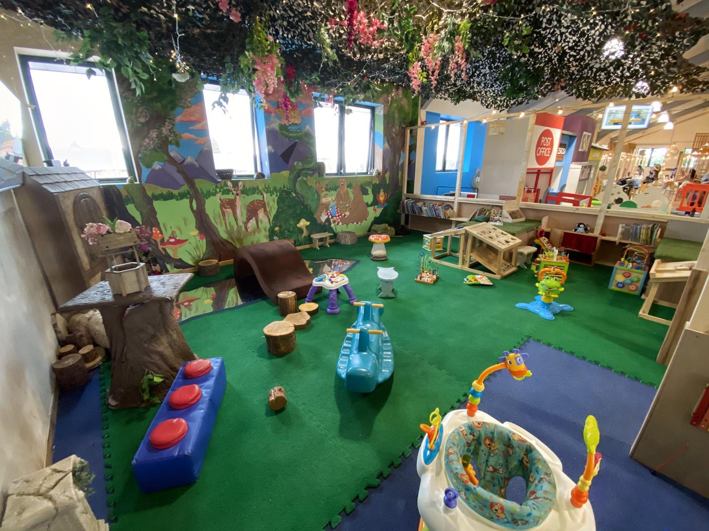 An event venue with artificial grass flooring, woodland mural, and sensory play equipment at The Hideaway Manchester.