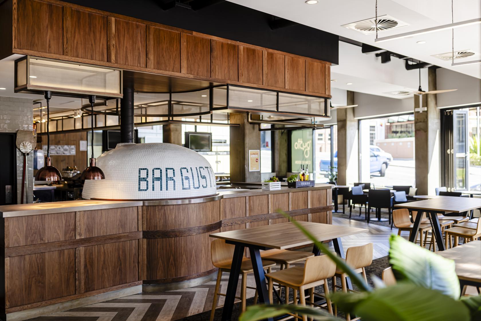 An event space in a restaurant with a wood-fired pizza oven, wooden tables, and large windows at Bar Gusto.