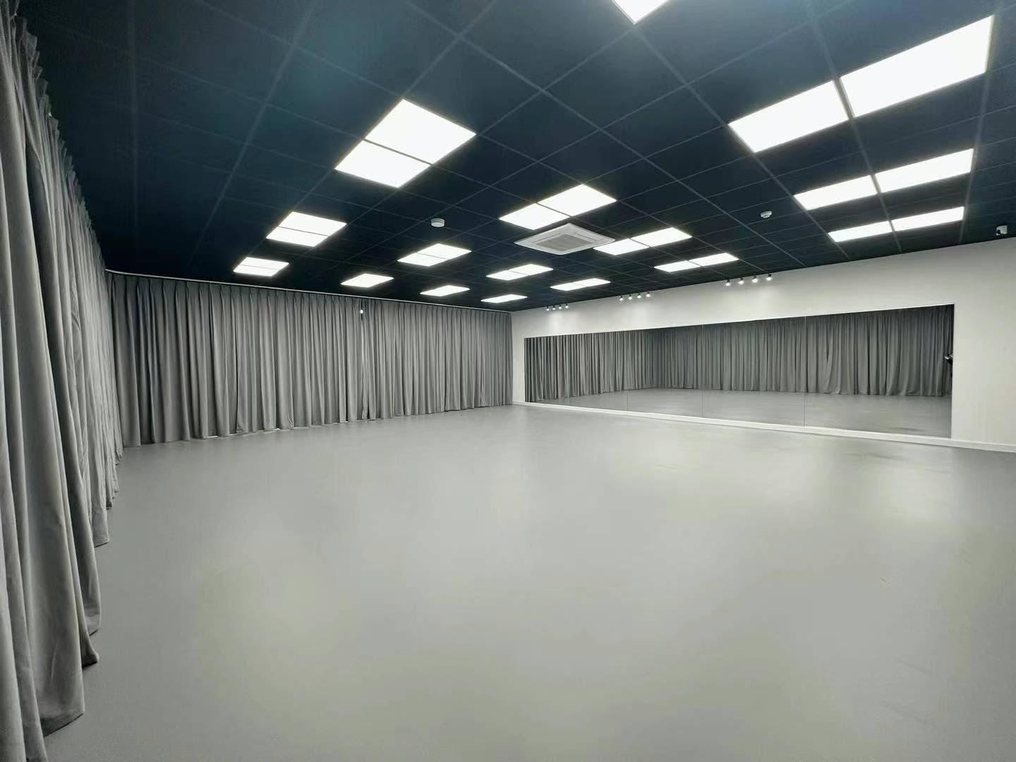 A dance studio with a spacious gray floor, full-length wall mirror, and ceiling lights at Manchester Chinese Academy of Dance.