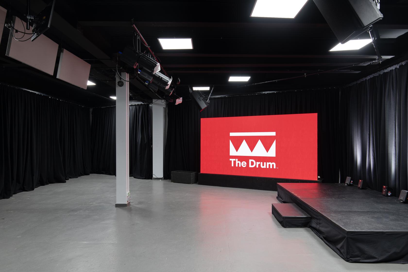 An event venue with a large LED screen, black draped walls, and a small stage at The Drum Labs.