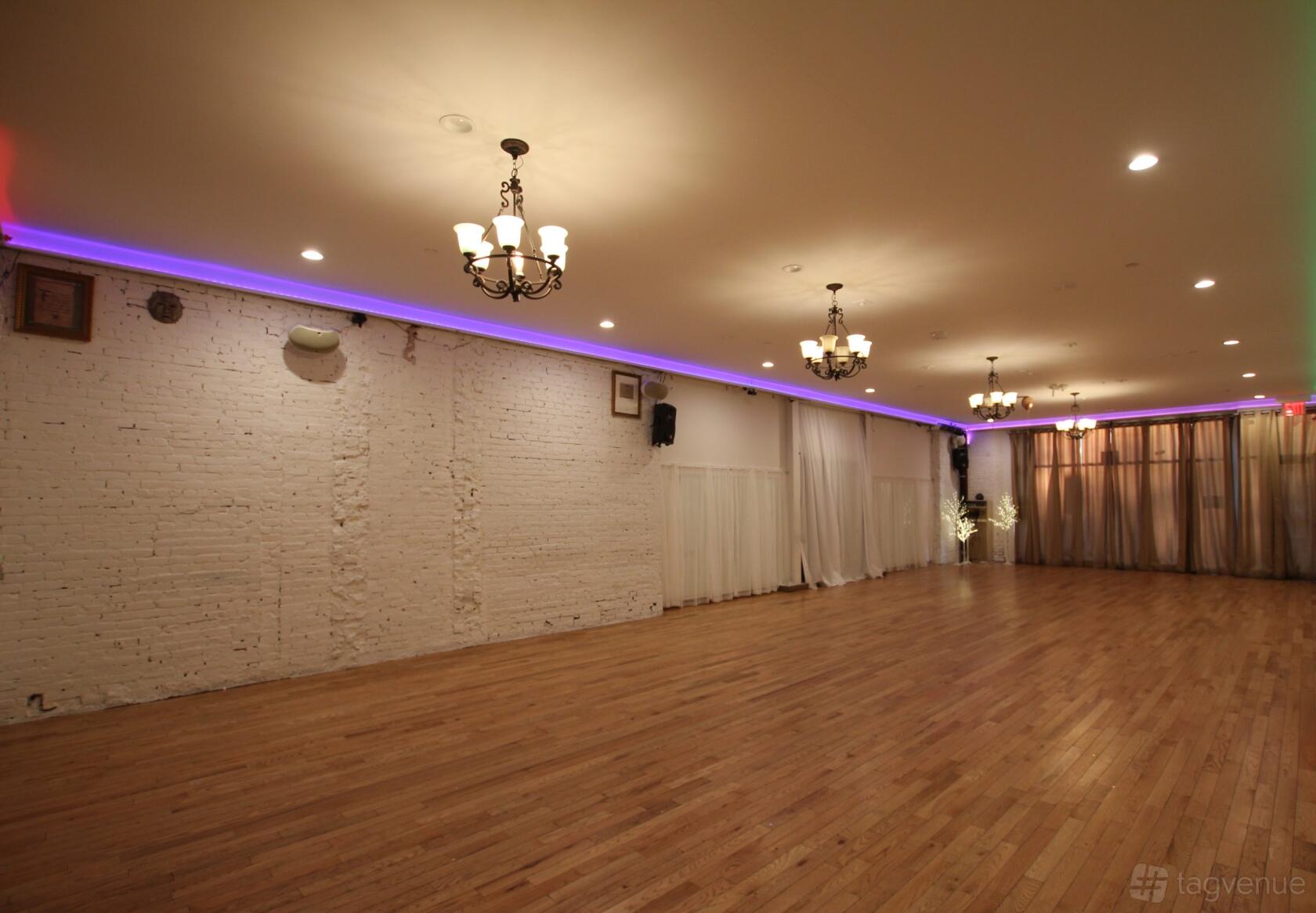 An event venue with exposed brick walls, hardwood floors, chandeliers, and floor-to-ceiling curtains at Space Bushwick.