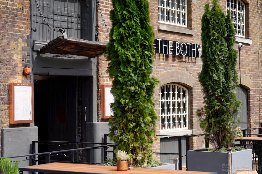 An outdoor pub area with brick walls, tall potted evergreens, and patio tables at The Sipping Room.