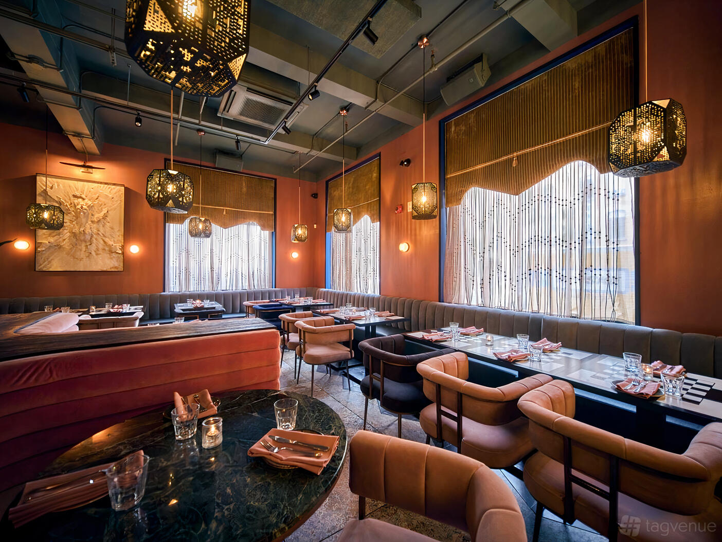 A restaurant with velvet banquette seating, marble tables, and geometric pendant lights at Silent H.