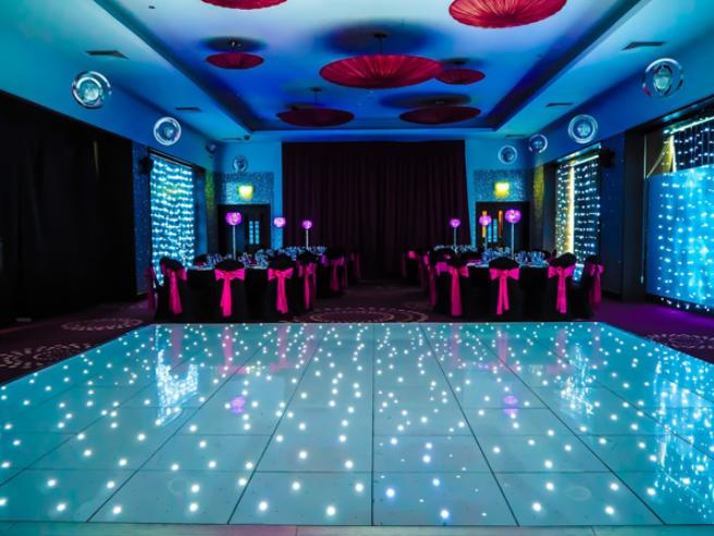 A function room with an LED-lit dance floor, round tables with pink sashes, and curtain backdrop at Alea Casino Glasgow.
