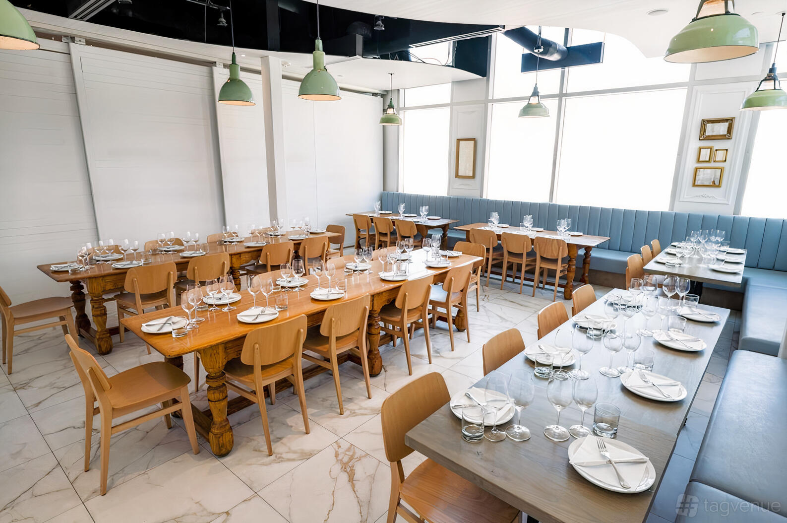 A restaurant dining room with long wooden tables, light wood chairs, and large windows at Nodo Liberty.