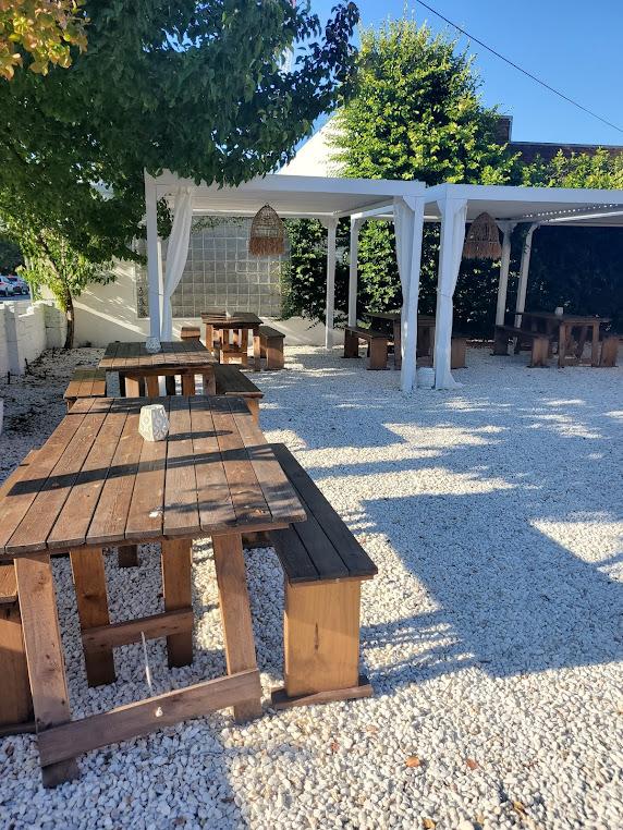A cafe terrace with wooden picnic tables on white gravel beneath a pergola at Lennox Cafe.