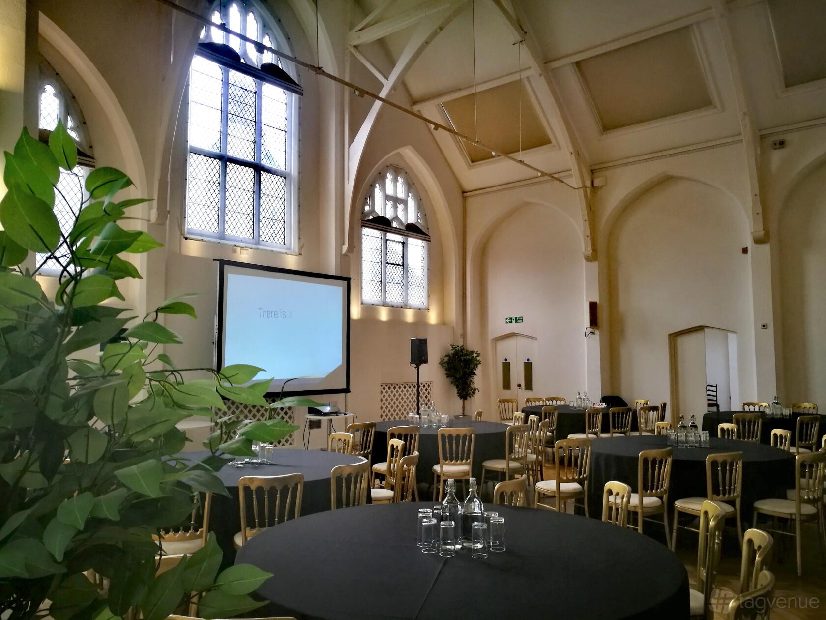 A hall with arched stained glass windows, vaulted ceilings, and round tables set for events at The Old Library.
