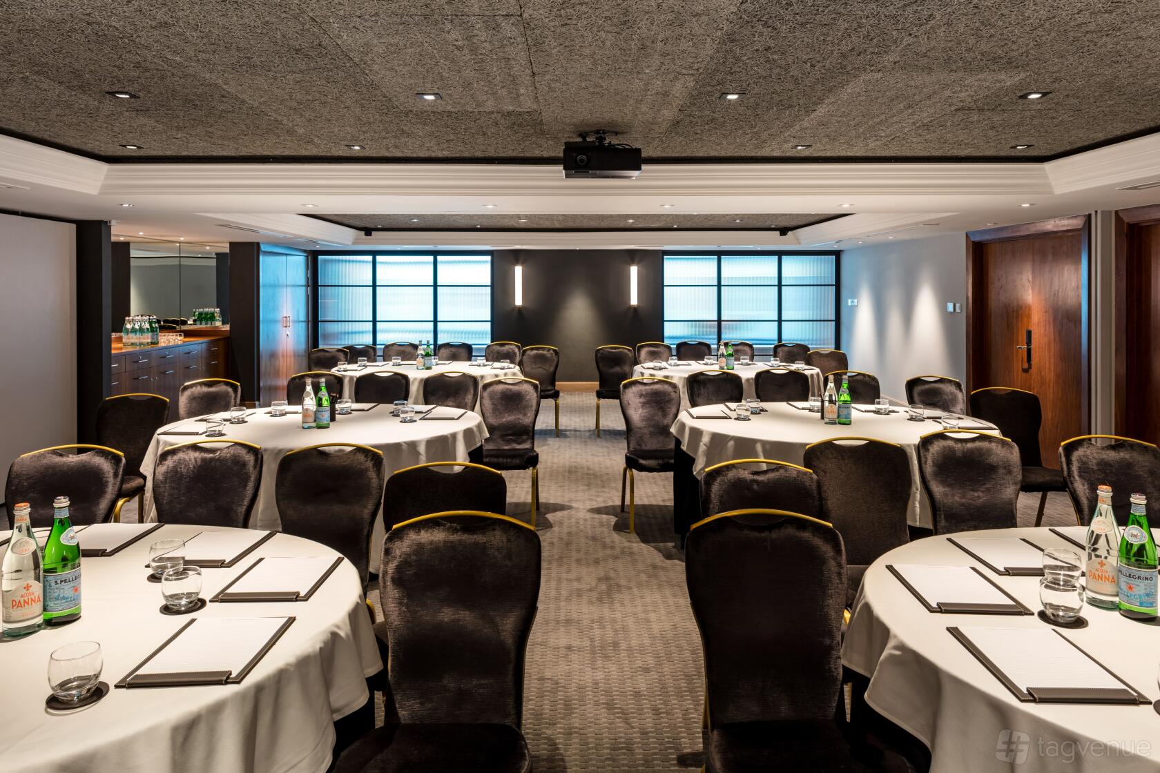 A hotel hall with round tables set with notepads and water bottles, velvet chairs, and soft lighting at The Edwardian Manchester.