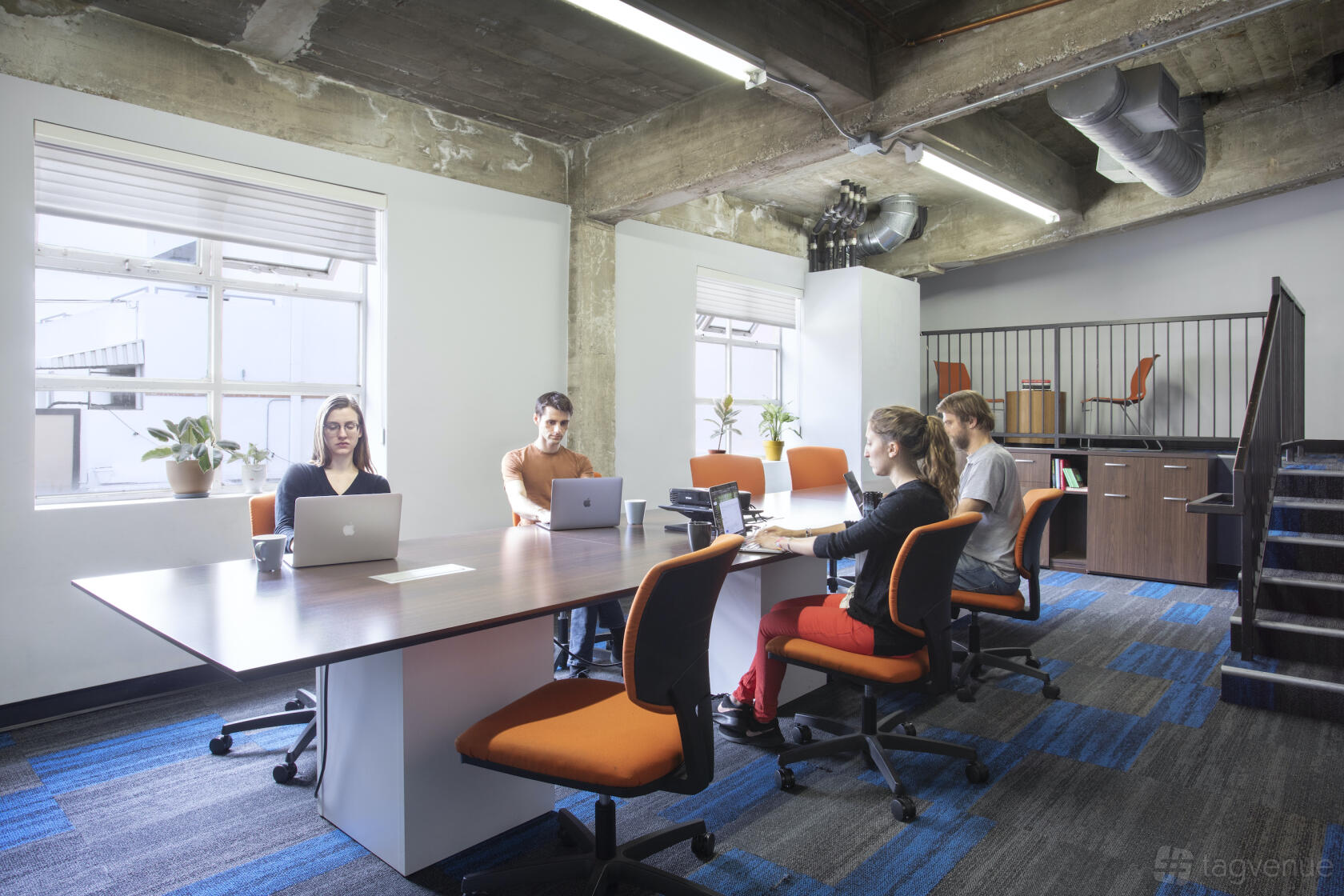 A meeting room with long tables, orange office chairs, large windows, and exposed concrete ceiling at BLANKSPACES Culver City.