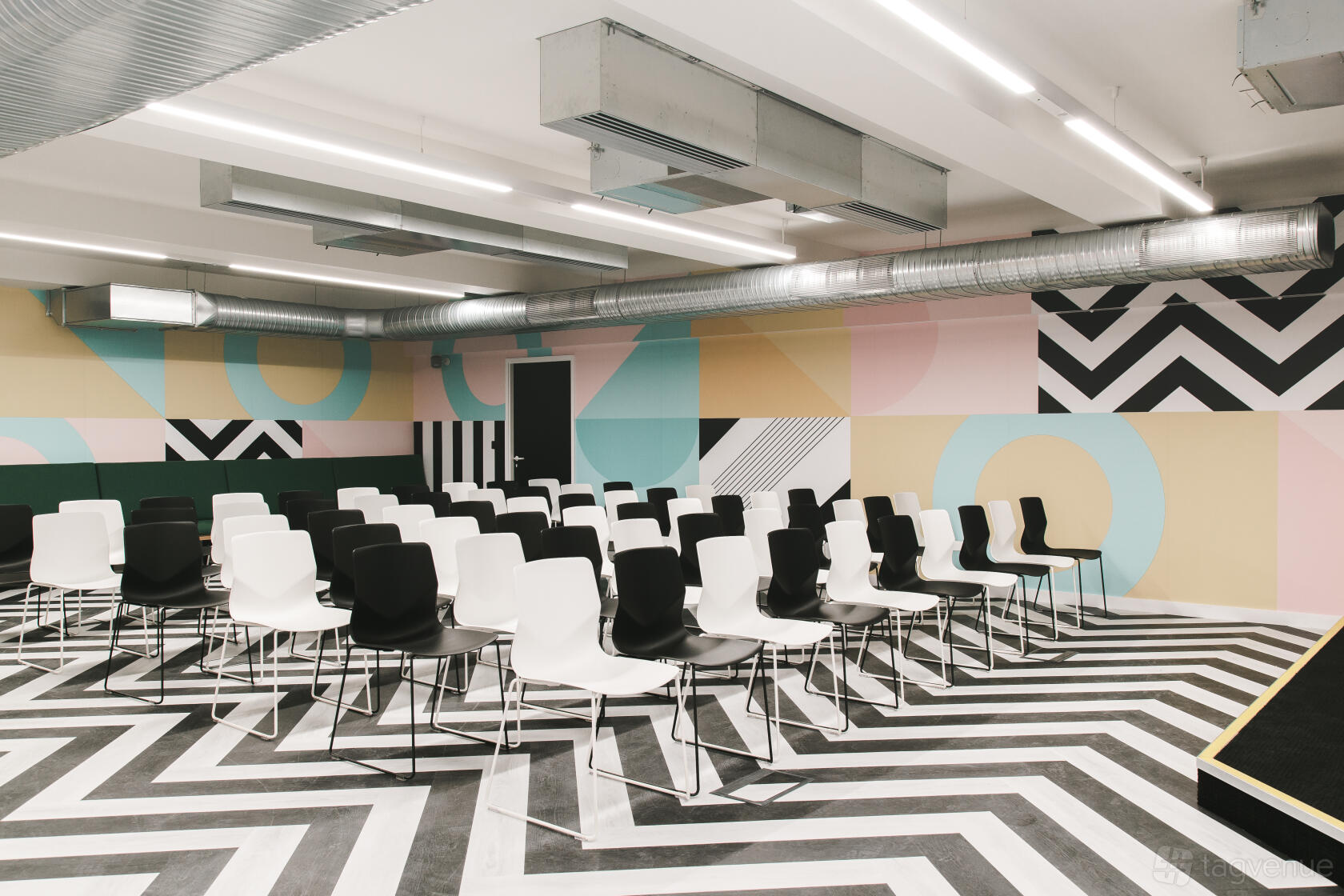 An event space with geometric wall art, chevron flooring, and rows of black and white chairs at Huckletree Ancoats.