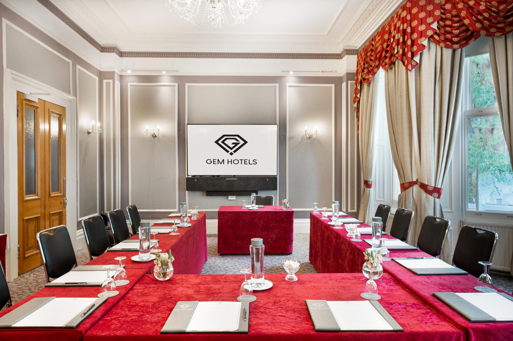 A hotel meeting room with U-shaped tables draped in red cloth, chandeliers, and tall windows at Strathmore Hotel.