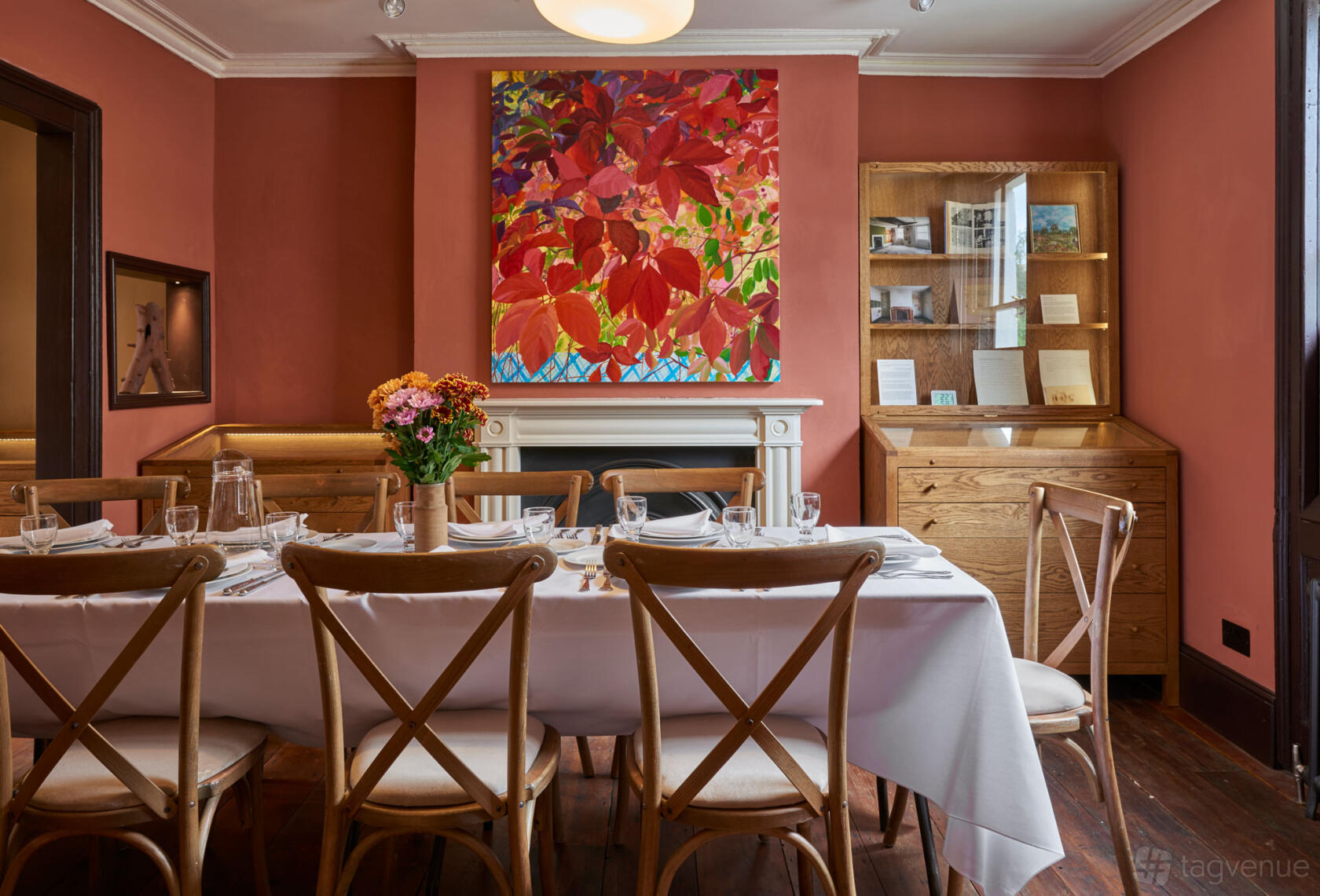 An art gallery room with coral walls, a large colorful painting above a fireplace, and a dining table with white linens at Van Gogh House.