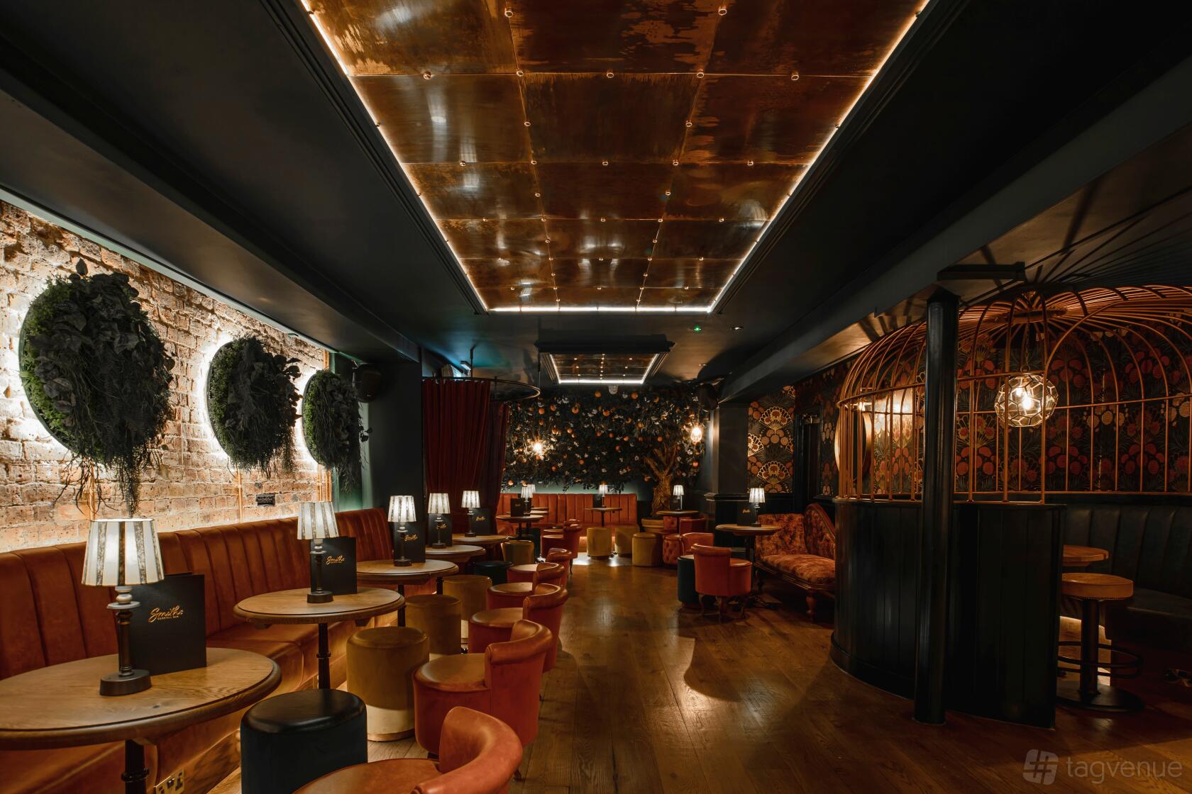 A cocktail bar with exposed brick walls, round tables, velvet seating, and ambient lighting at Smiths Cocktail Bar.