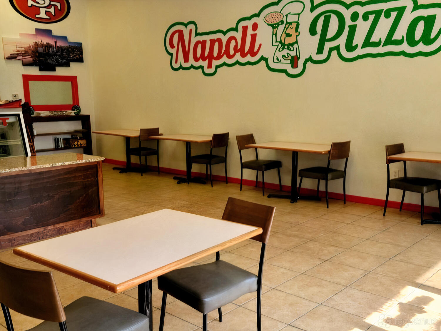 A restaurant with tiled floors, wall art, and simple wooden tables with chairs at Napoli Pizza.