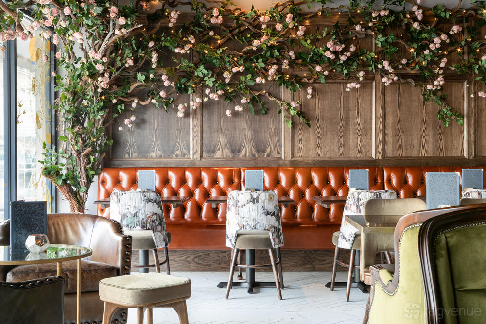 A lounge with tufted orange banquette seating, floral-patterned chairs, wood paneling, and greenery at The Lost & Found Bristol.