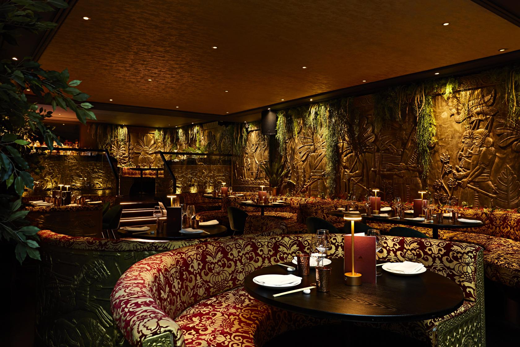 A restaurant with curved banquette seating, candlelit tables, and carved gold walls at Gilgamesh London Covent Garden.