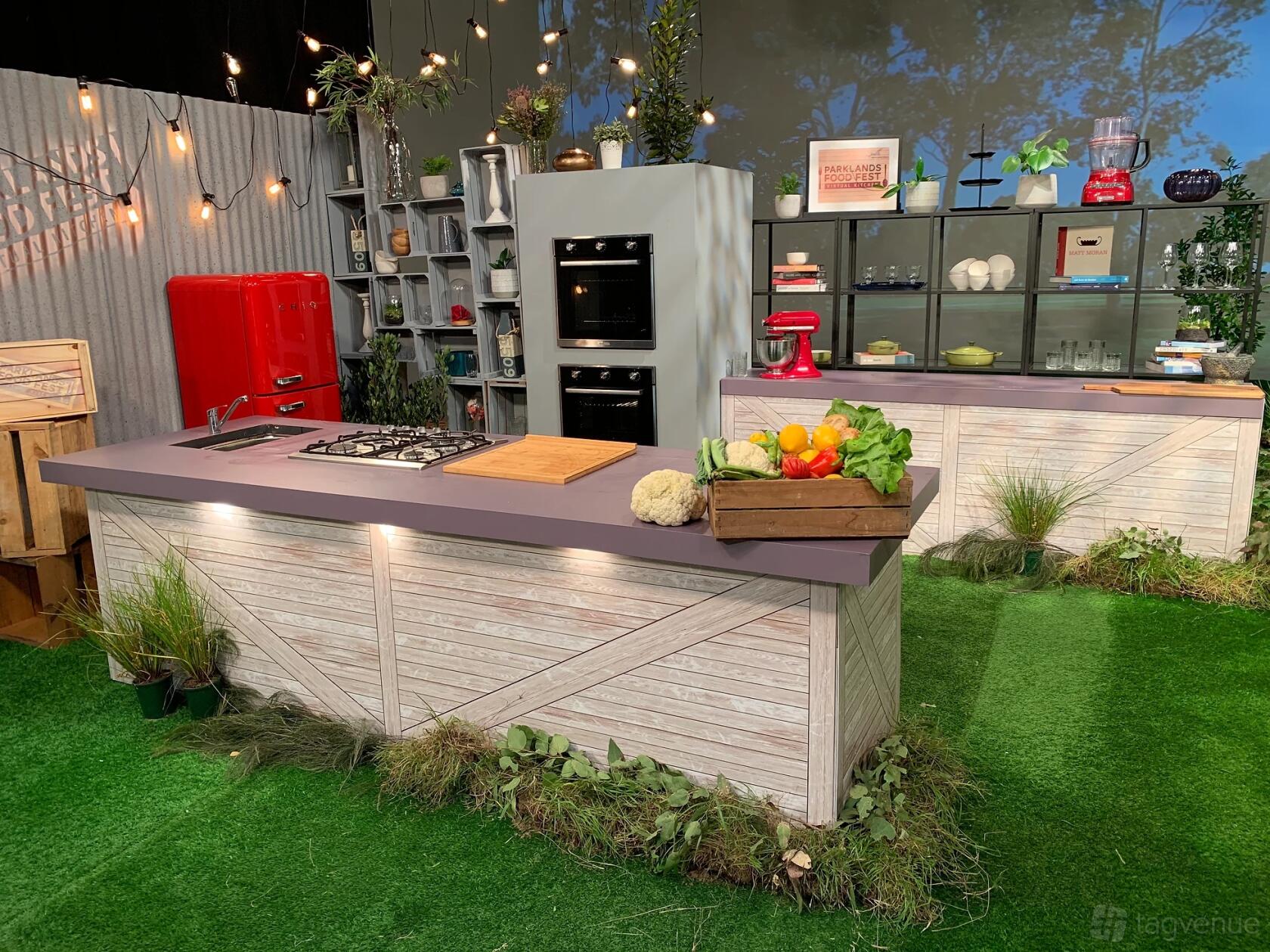 A kitchen studio with an island cooktop, red retro fridge, open shelving, and potted plants at Damn Good Productions.