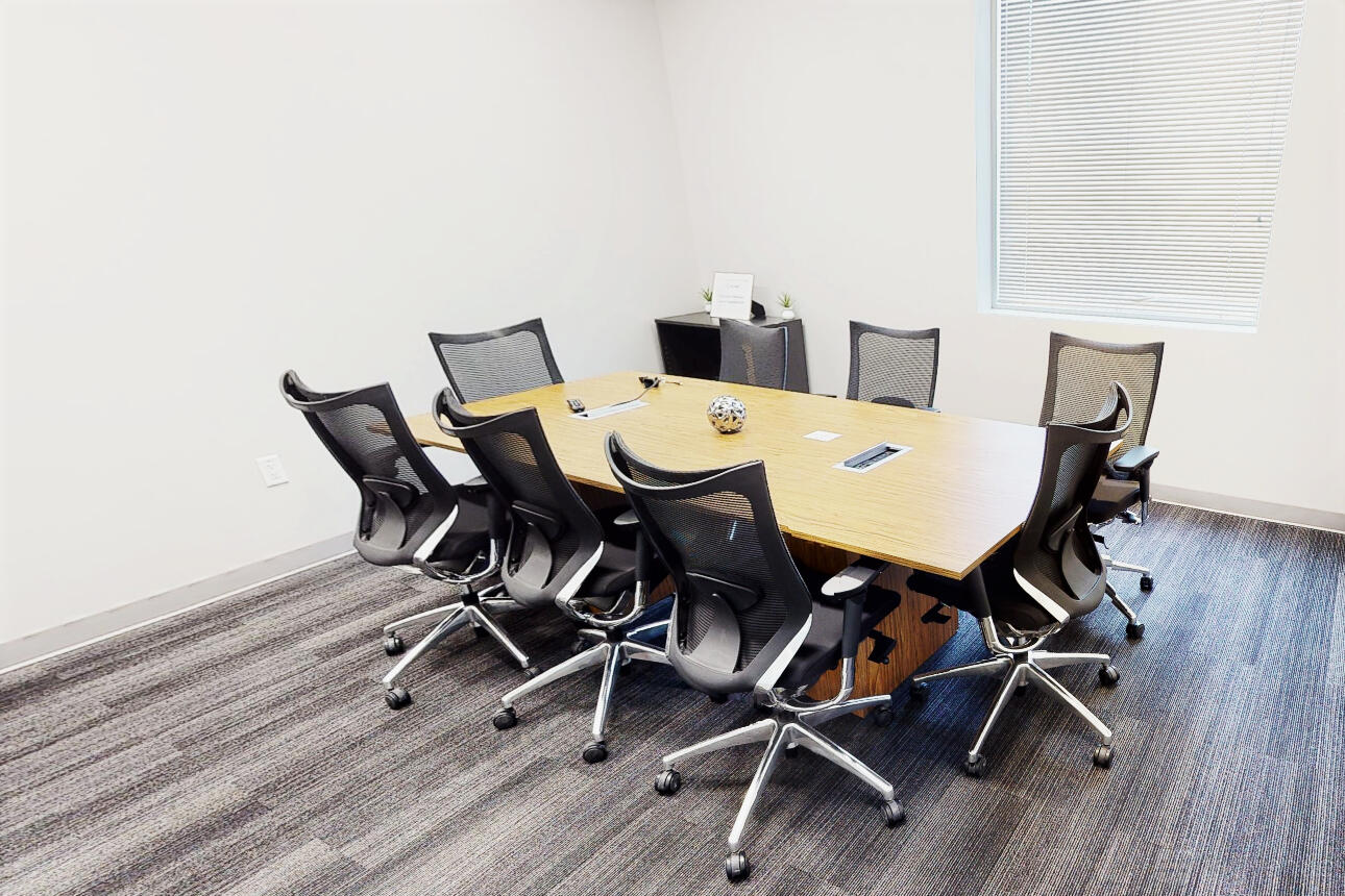 A meeting room with a rectangular wooden table, black mesh chairs, and large window at MedtoMarket Event and Conferencing Center.