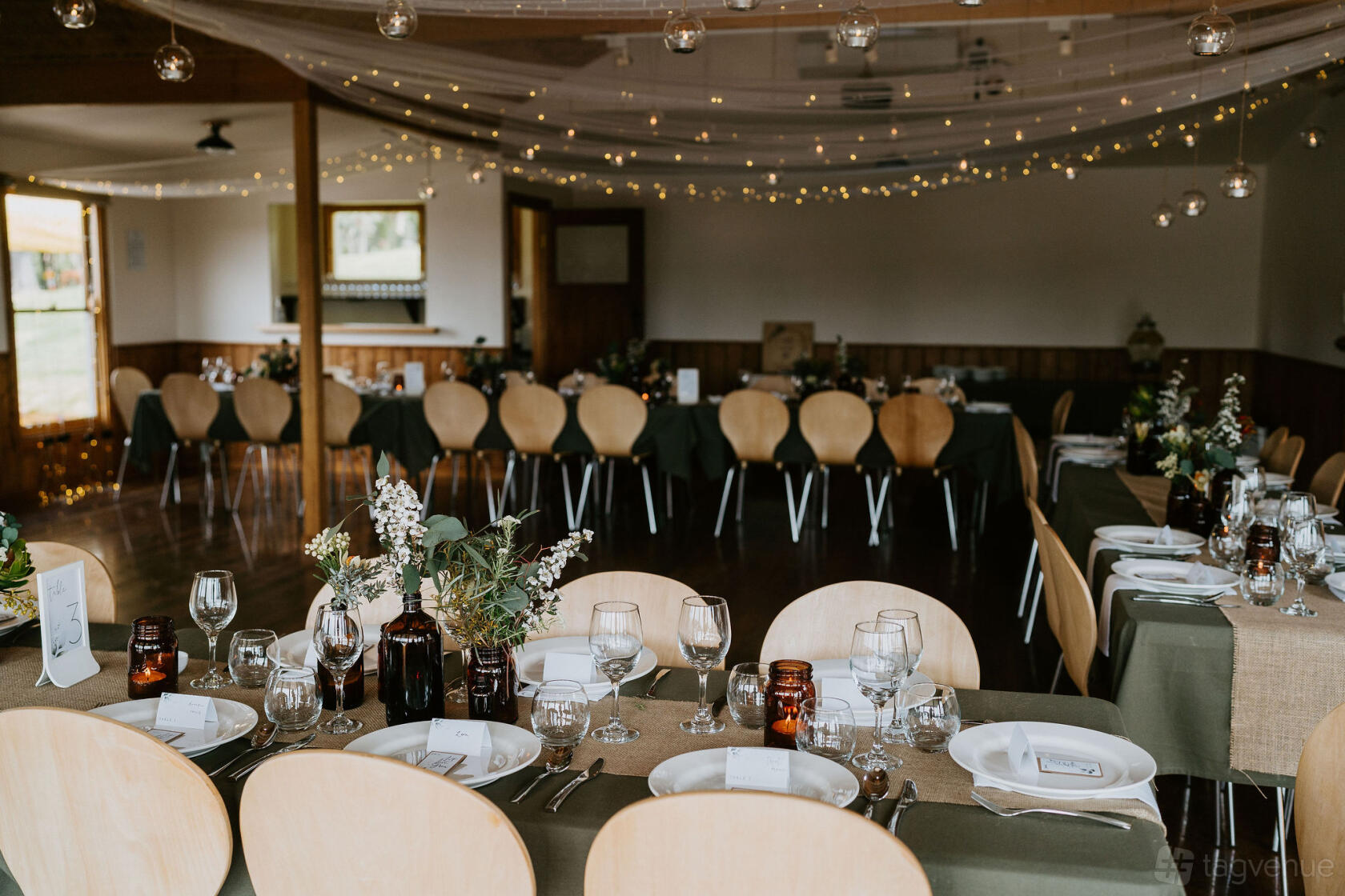 An indoor hotel event space with long tables, rustic decor, draped fabric ceiling, and hanging fairy lights at King Parrot Cottages and Event Centre.