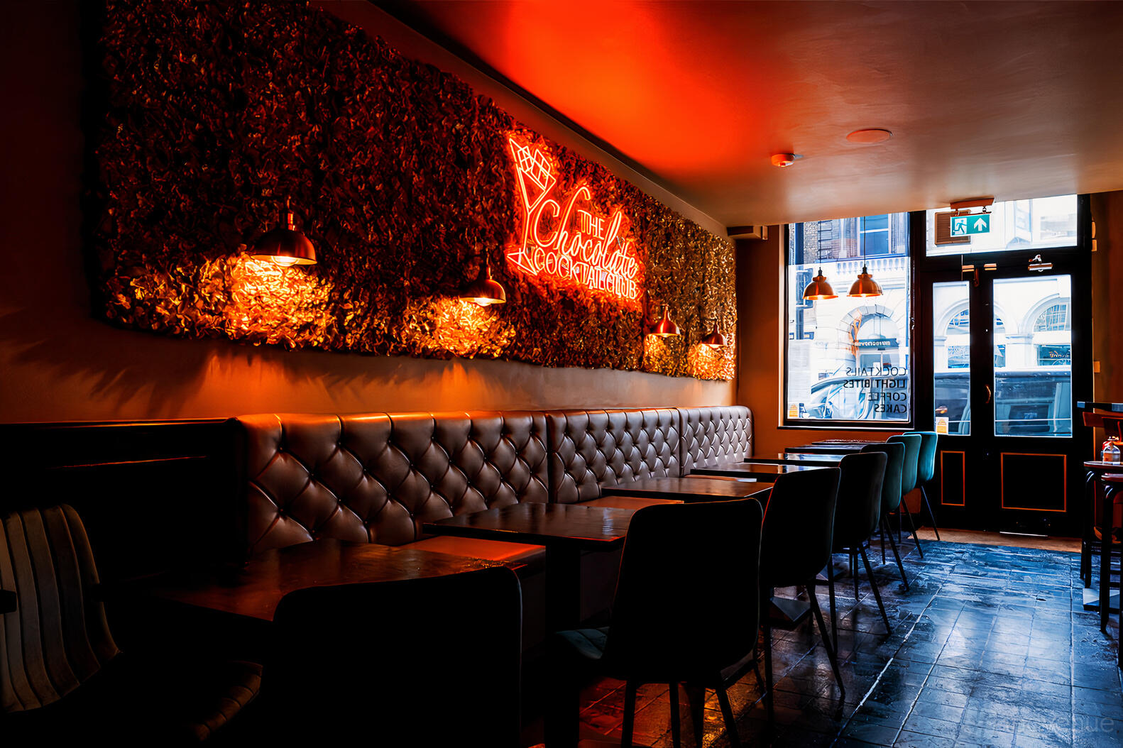 A cocktail bar with tufted banquette seating, neon sign, and wall greenery at The Chocolate Cocktail Club.