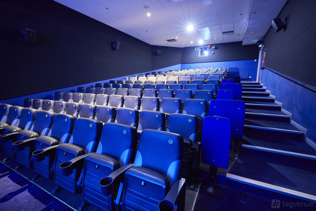 A cinema auditorium with tiered rows of blue cushioned seats and aisle lighting at ODEON Tottenham Court Rd.