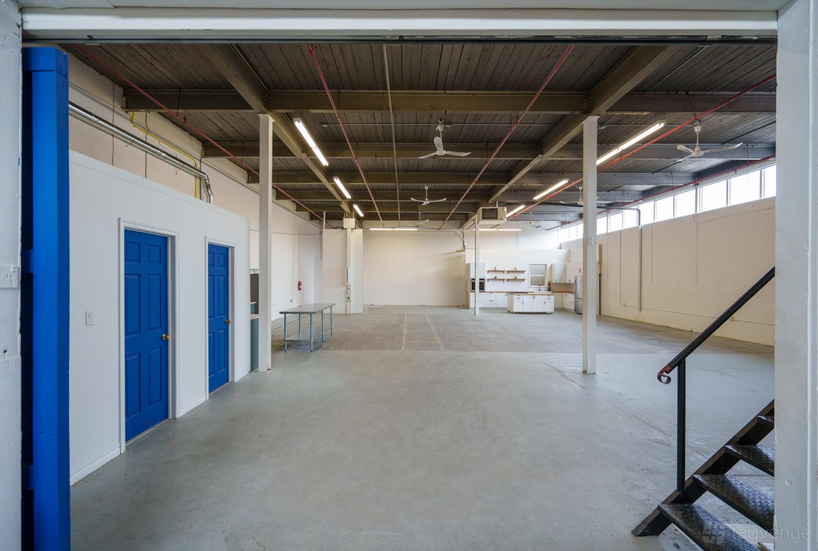 A spacious photo studio with high ceilings, exposed beams, blue doors, and concrete floors at Canteen Studios.