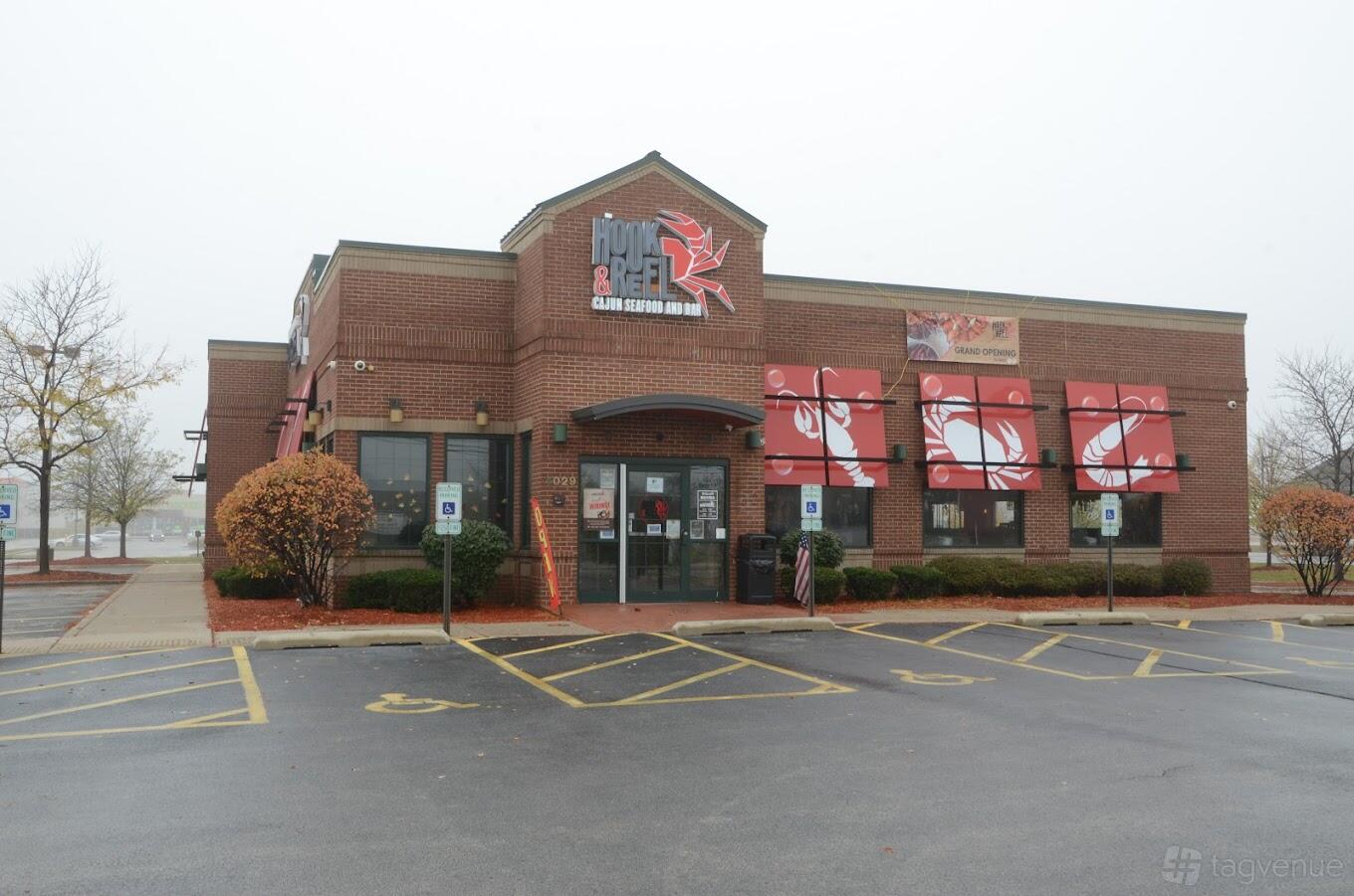 A restaurant with red brick exterior, large red awnings, and ample parking at Hook & Reel- Country Club Hills.