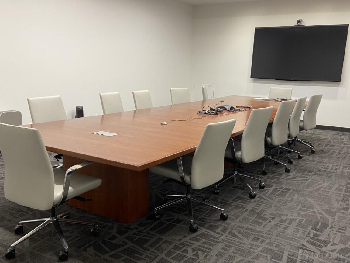 A boardroom with a long wooden conference table, white swivel chairs, and a wall-mounted screen at Roundhouse Market & Conference Center.