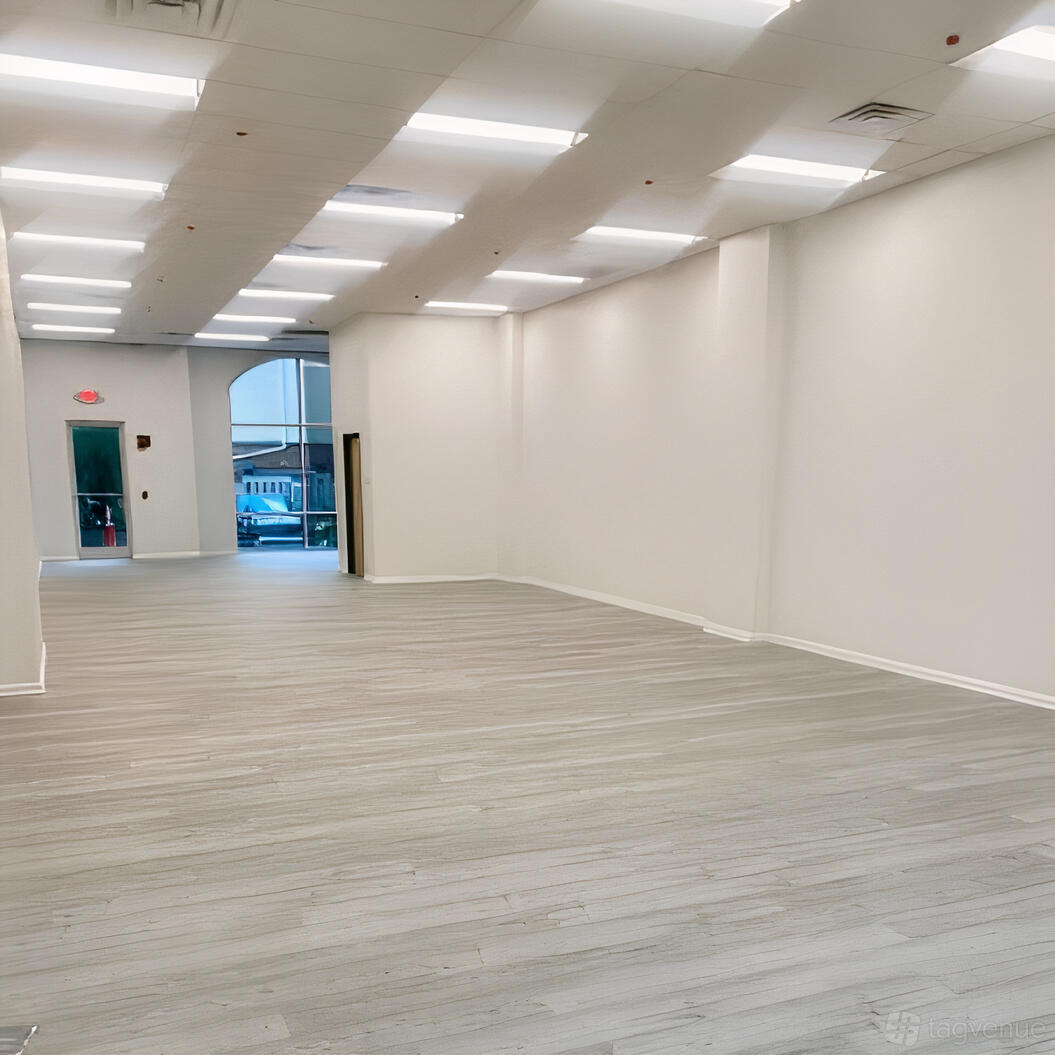 An event venue with light wood floors, white walls, and bright overhead strip lighting at Events By Meloni Nicole.