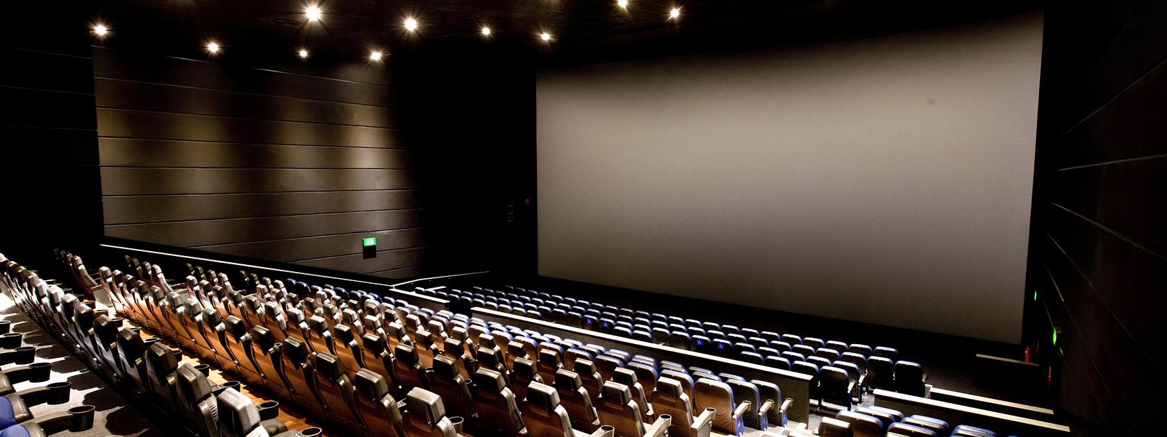 A cinema screening room with tiered rows of cushioned seats facing a large projection screen at ODEON Trafford Centre.