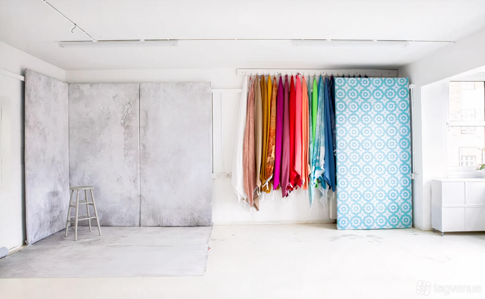 A photo studio with seamless backdrops, a collection of colorful fabric rolls, and a metal stool at SET Studio.