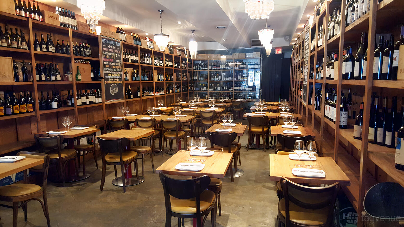 A restaurant with wooden tables, shelves lined with wine bottles, and chandeliers at Salt - Toronto.