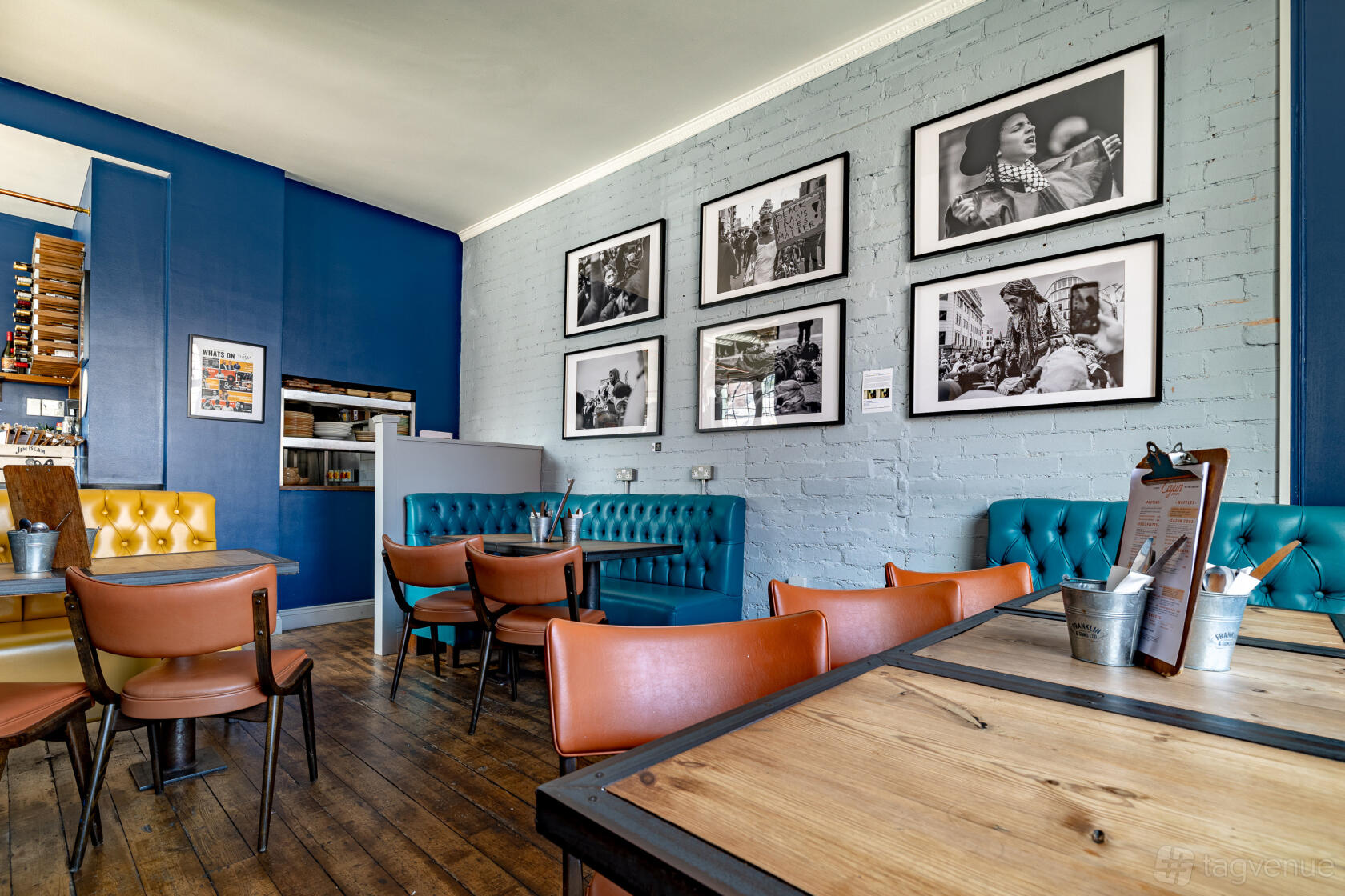 An event space in a bar with teal tufted sofas, framed black and white photos, and wooden floors at Temper and Brown.