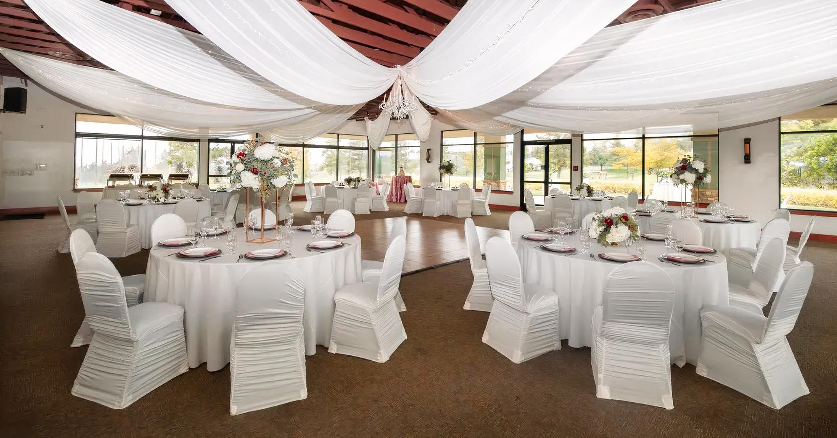 An event venue with draped white fabric ceiling, large windows, and round tables with white linens at The Pavilion at Chapman Ranch.