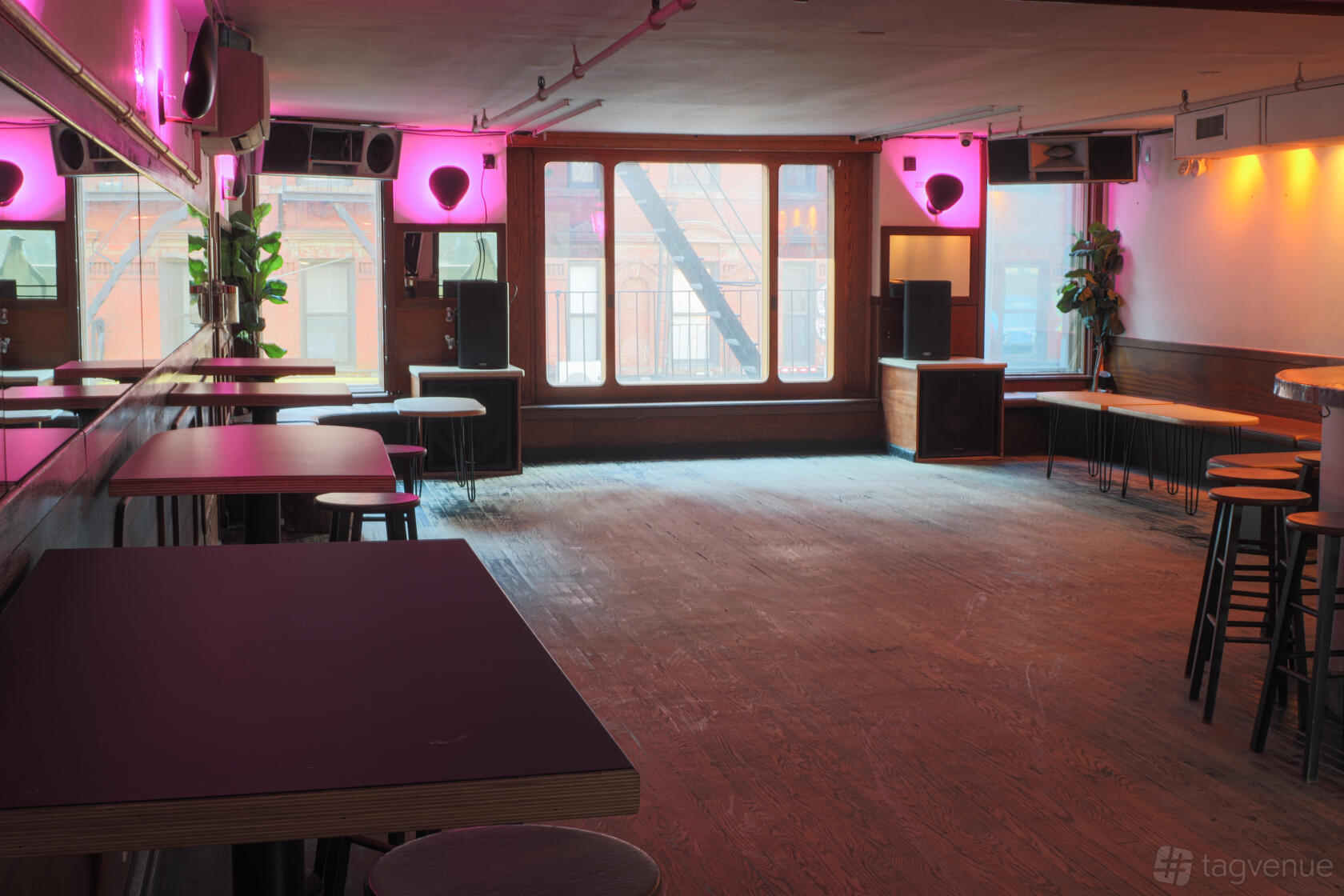 An event space with pink accent lighting, large windows, wooden floors, and bar tables at Piano's.