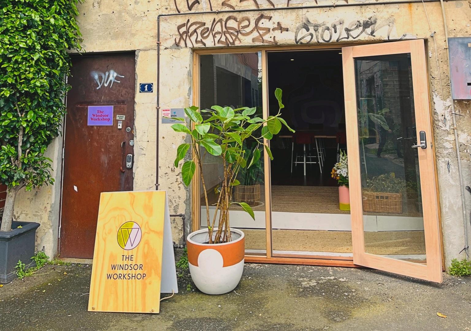 A versatile event space with a sliding glass door entrance, potted plant, and branded sign at The Windsor Workshop.