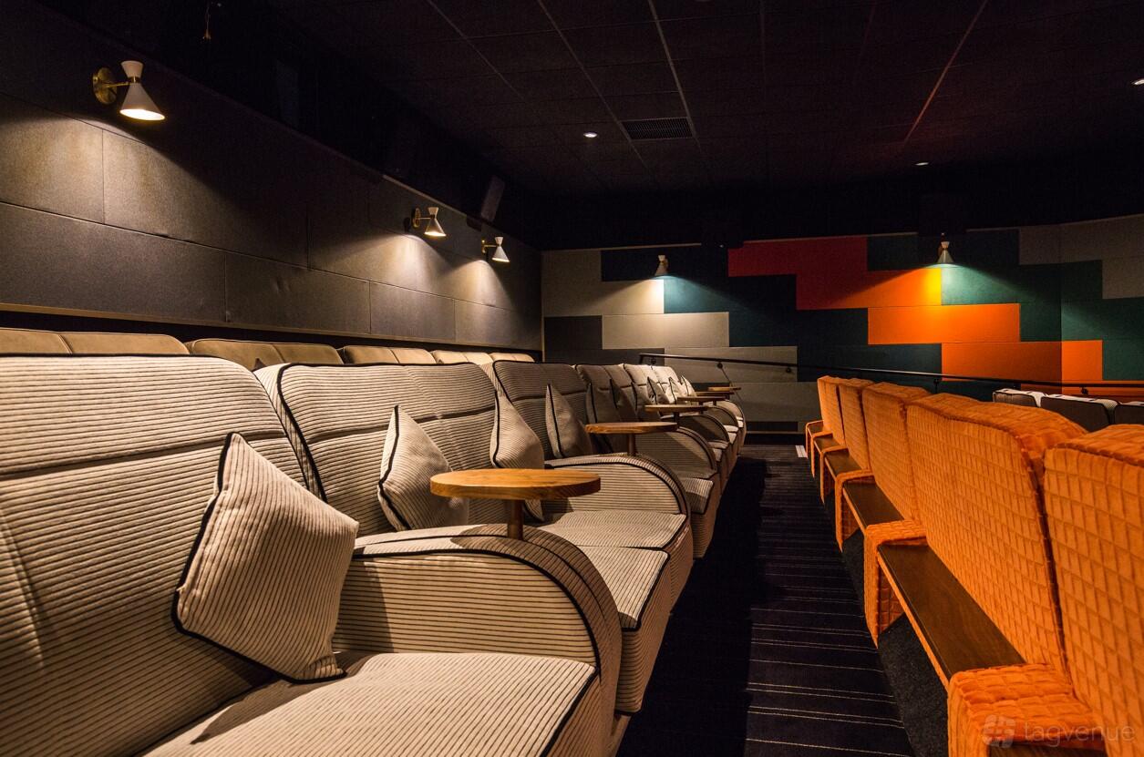 An auditorium with plush striped armchairs, small wooden tables, and geometric wall panels at Everyman Esher.