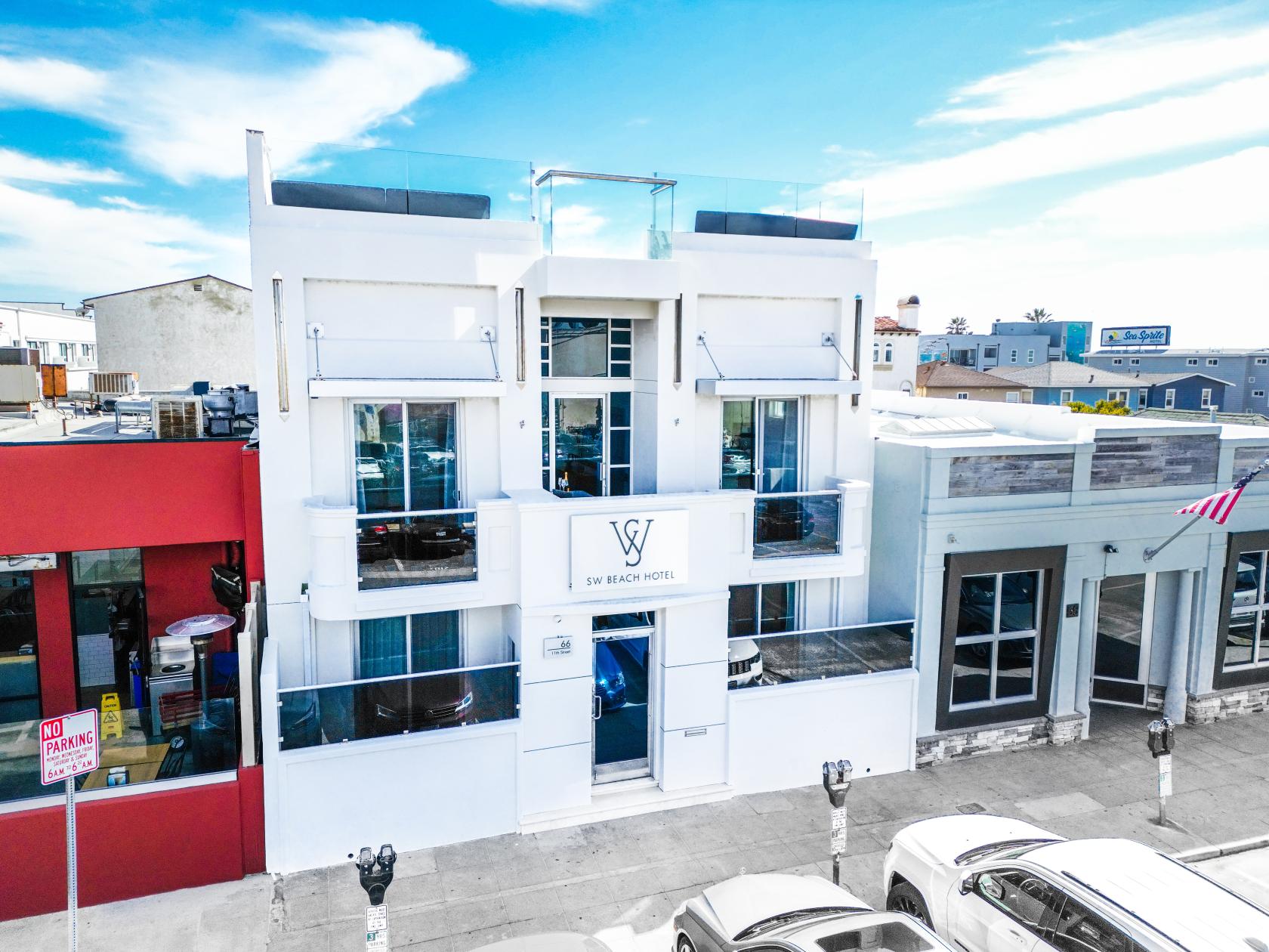 A white hotel rooftop with glass railings and a view of nearby buildings at SW Beach Hotel Rooftop.