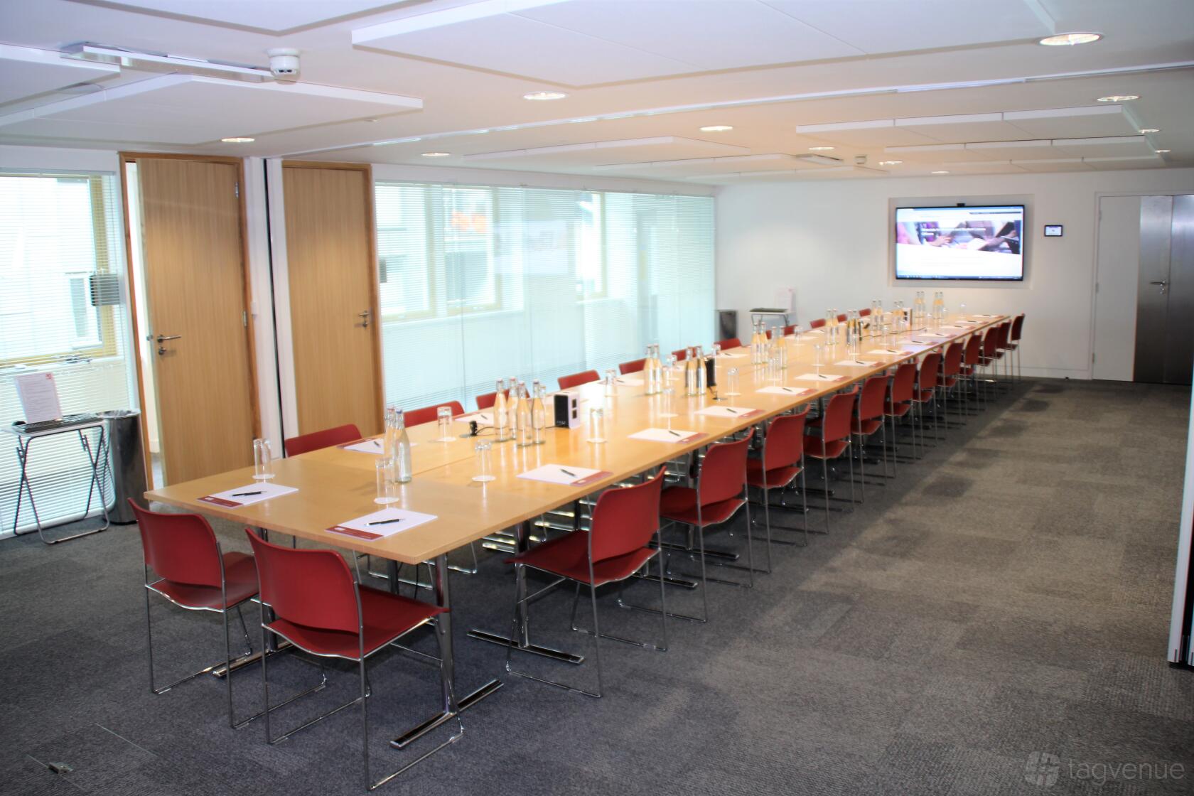 A meeting centre with a long conference table, red chairs, notepads, and a wall-mounted screen at 47-58 Bastwick Street.