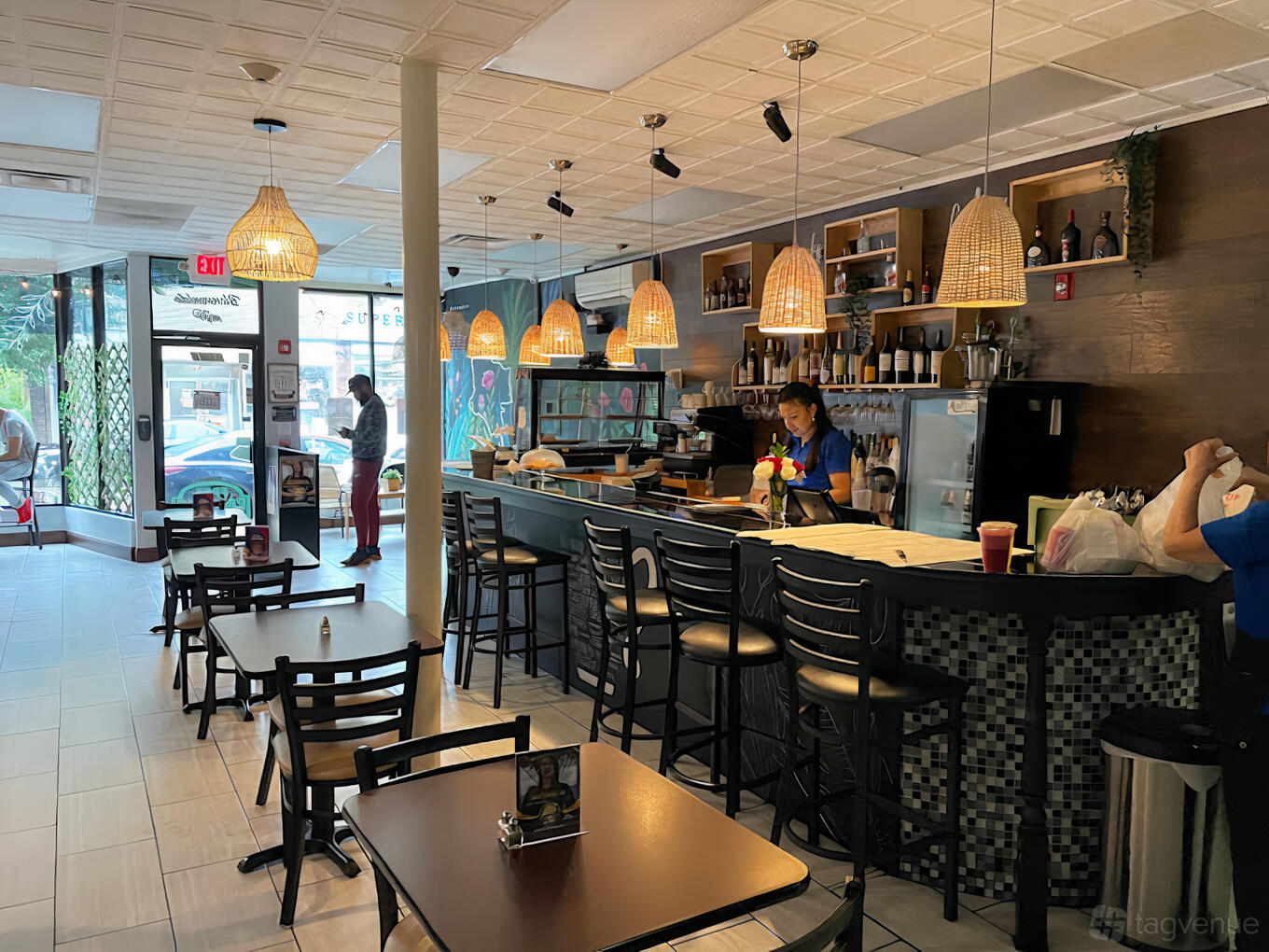 A restaurant with pendant lights, a tiled bar counter, wooden tables, and large front windows at Delicias Colombianas Hyde Park.
