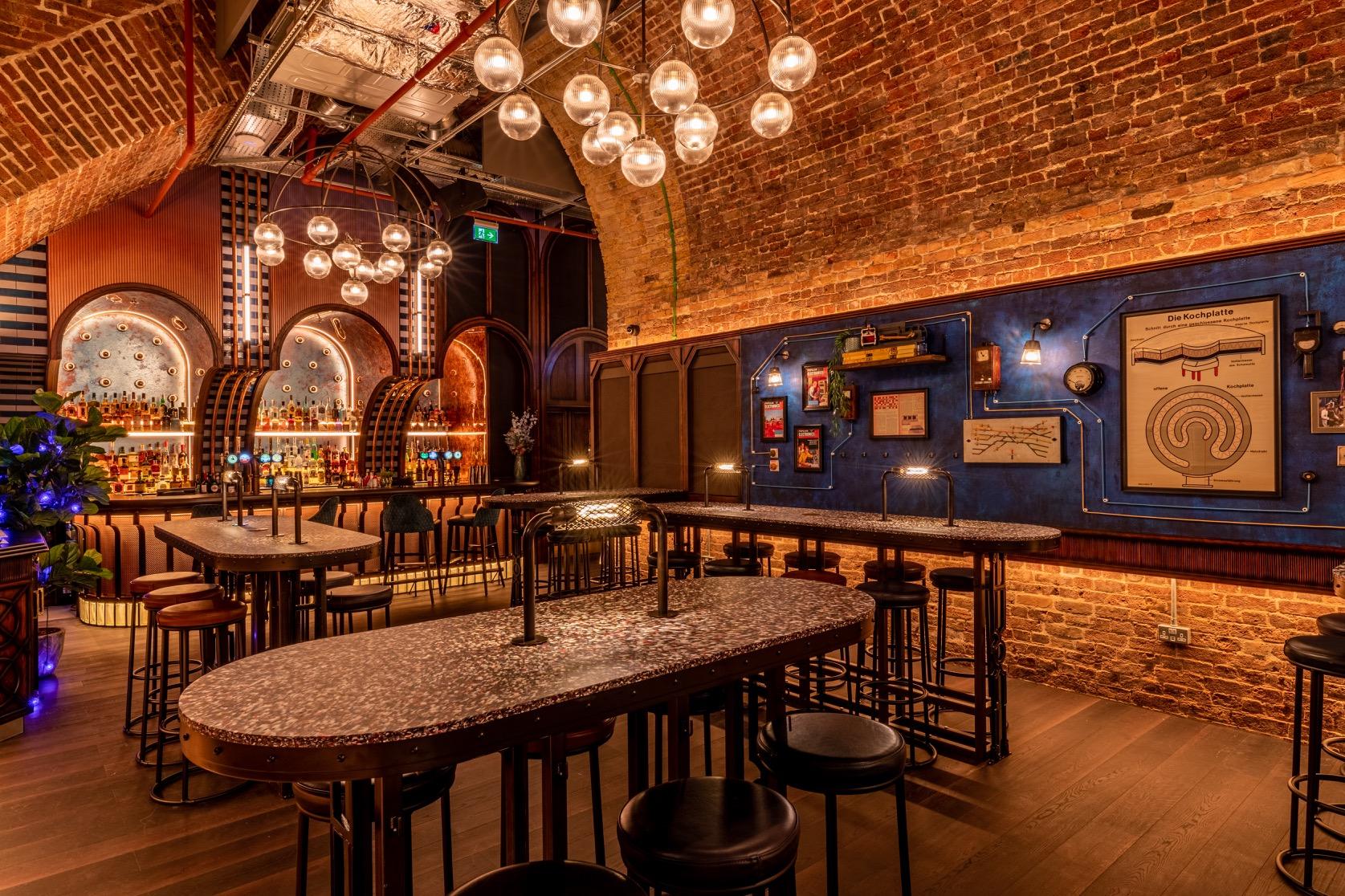 An event space in a cocktail bar with exposed brick walls, globe pendant lights, and terrazzo high tables at Electric Shuffle London Bridge.