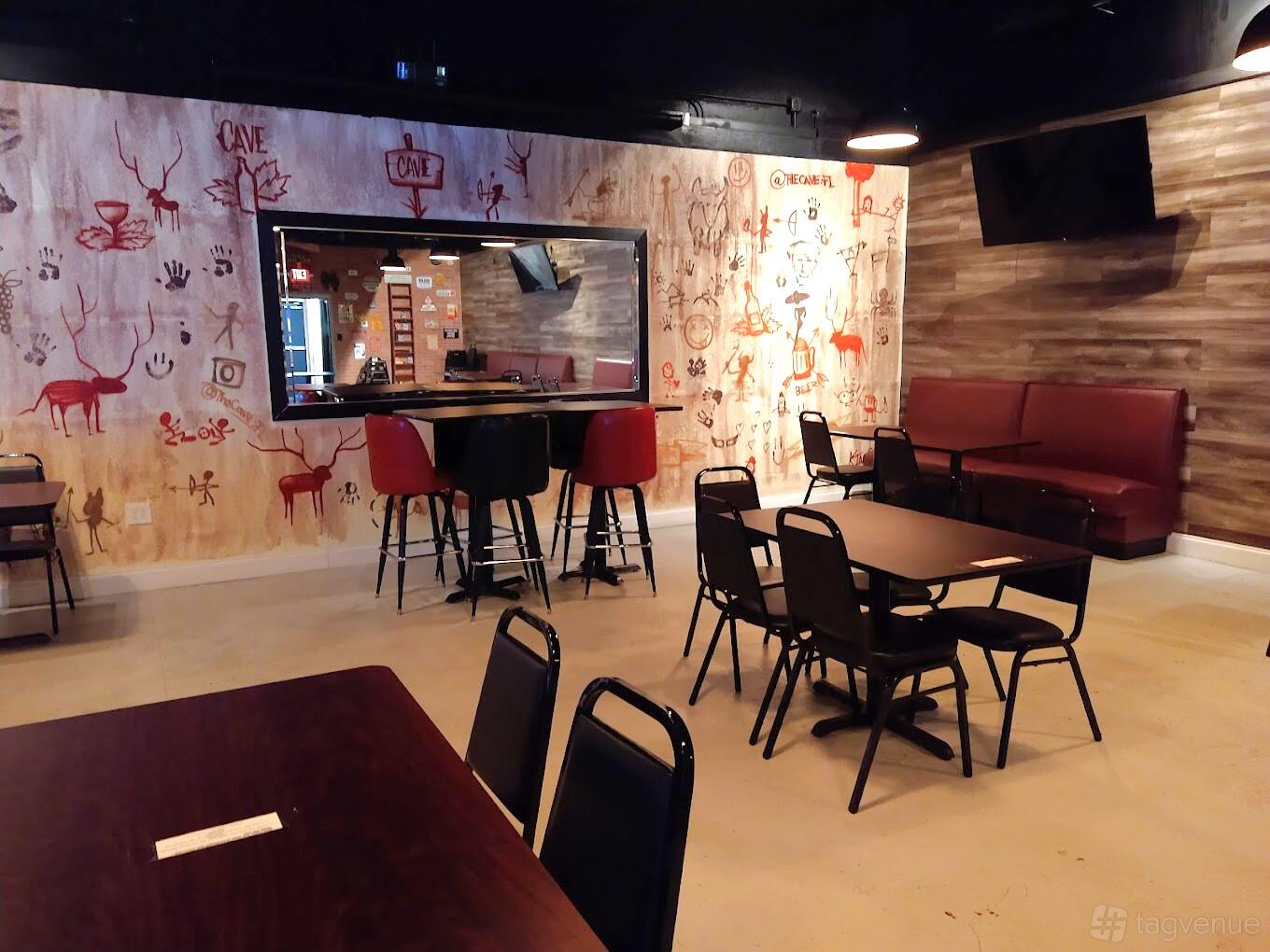 A restaurant with cave-inspired wall art, dark tables, and red cushioned seating at The Cave Restaurant and Bar.