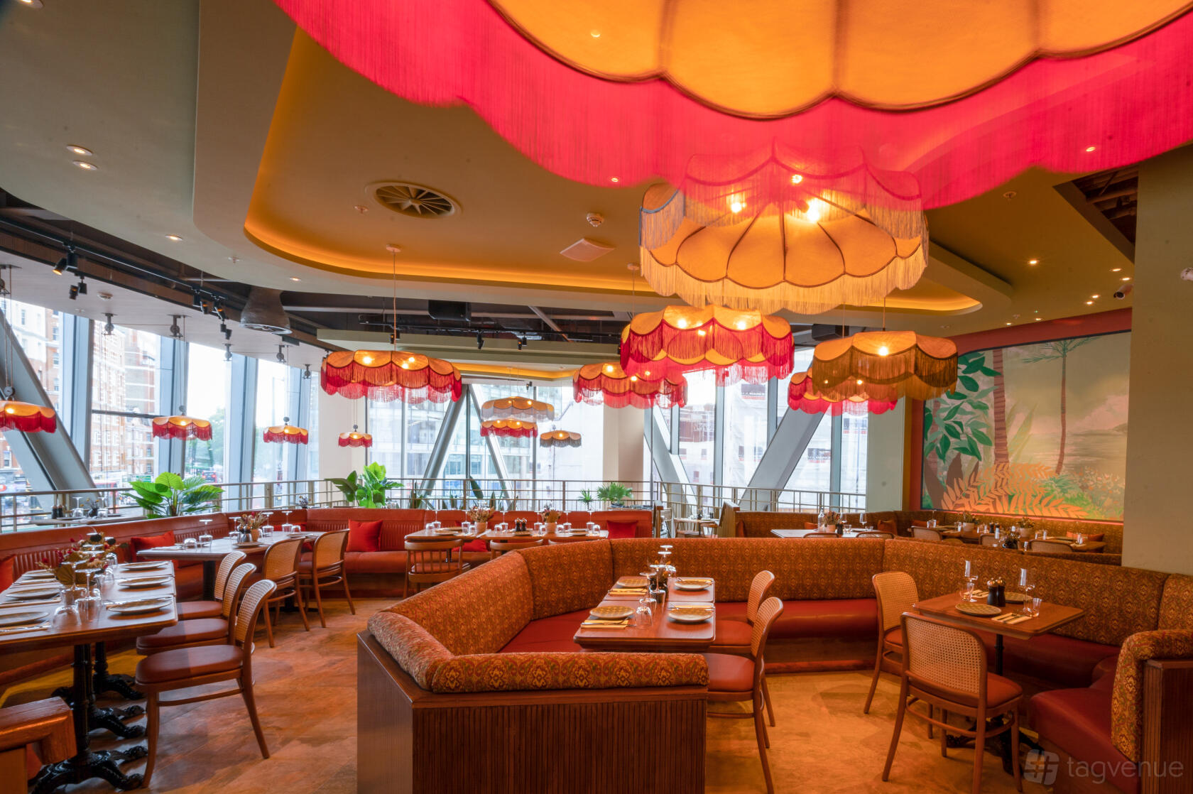 A bar with colorful hanging lamps, floor-to-ceiling windows, and patterned booth seating at The Palm House.