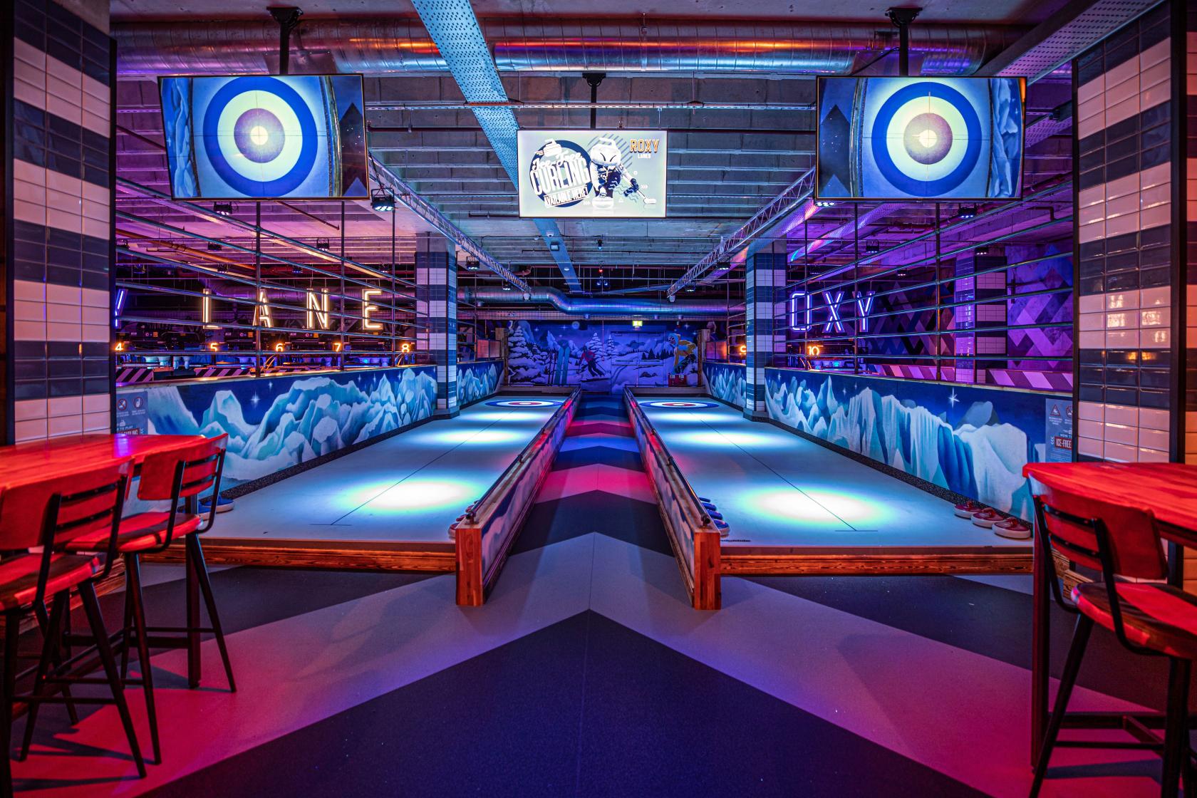 An event space in a bar with illuminated ice-free curling lanes and colorful wall murals at Roxy Lanes Leeds The Light.