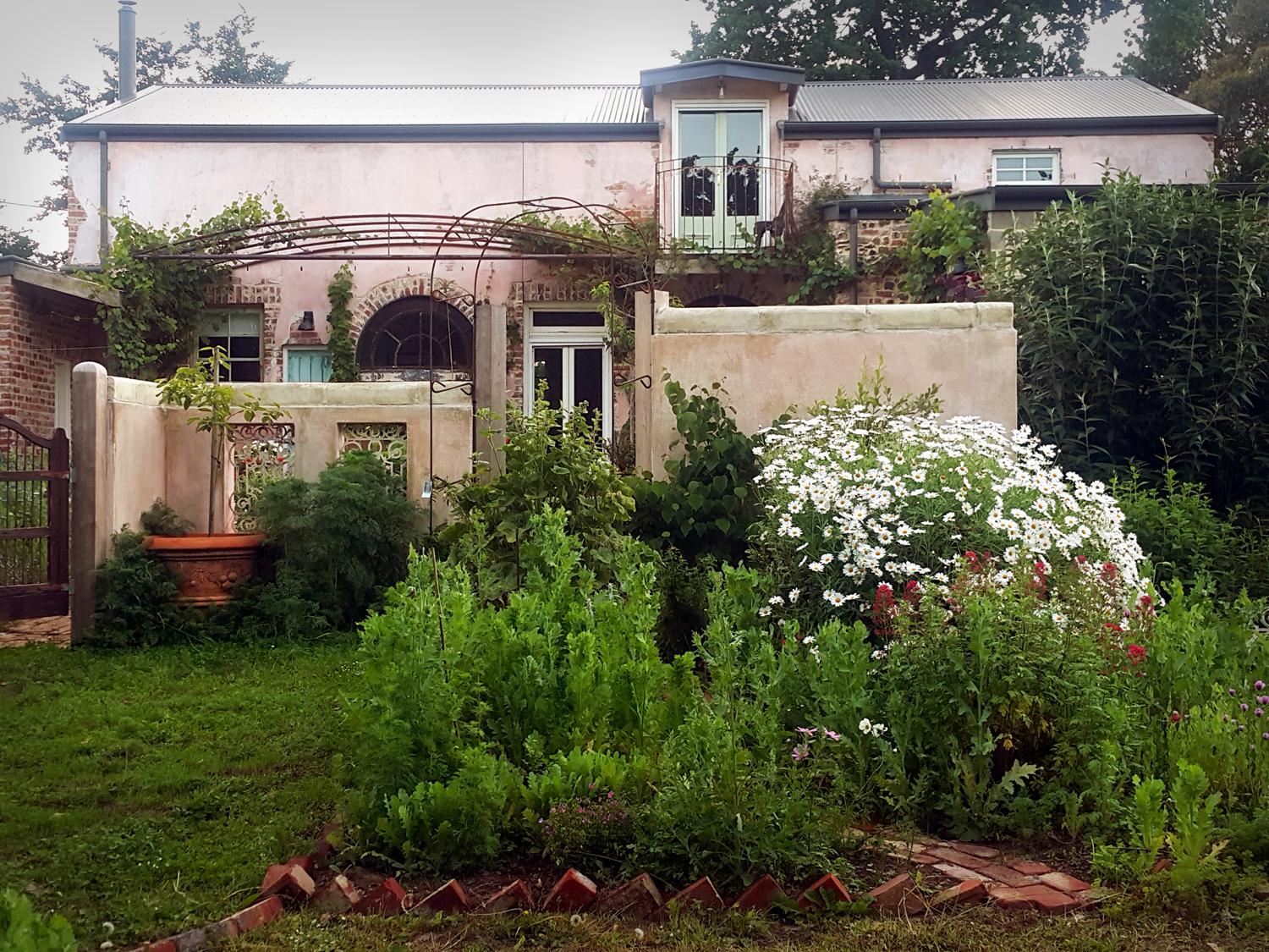 A country house with a pink plaster exterior, arched windows, and a lush garden at The Potterage.