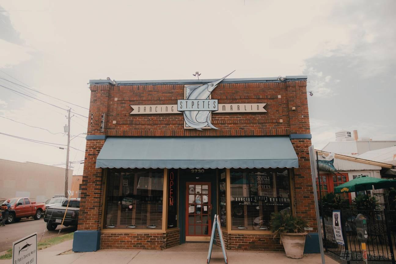 A restaurant with a brick facade, blue awning, and large fish sign above the entrance at St. Pete’s Dancing Marlin.